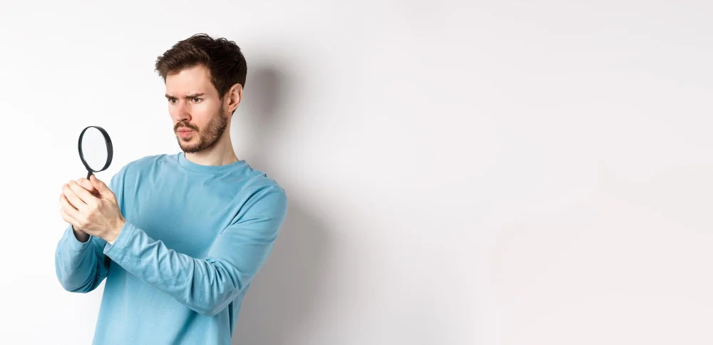 Mann im blauen Pullover betrachtet etwas genau mit einer Lupe.